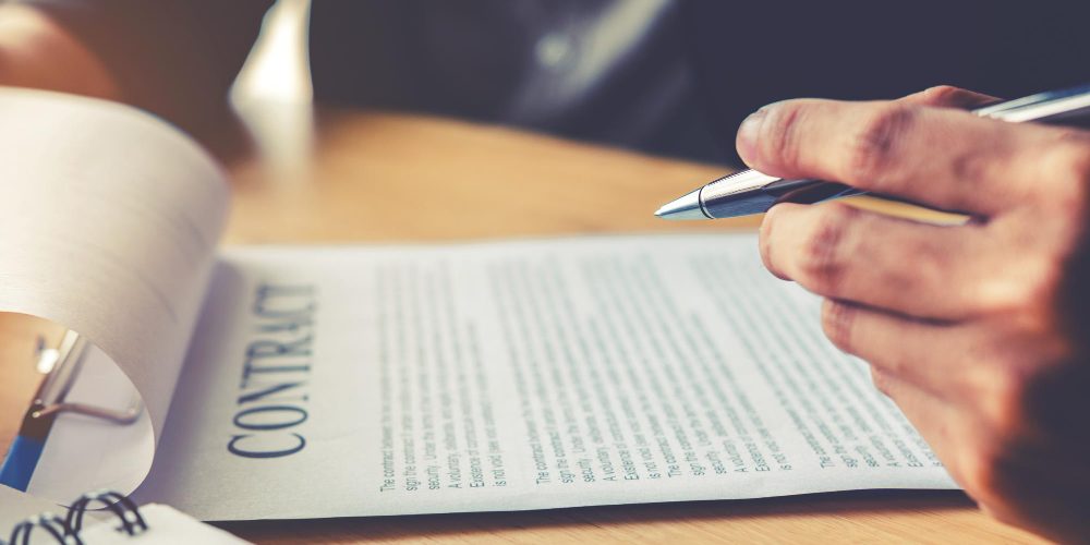 Main tenant un stylo au-dessus d’un contrat imprimé, symbolisant la gestion et la sécurisation des accès aux ressources ou dépôts logiciels.
