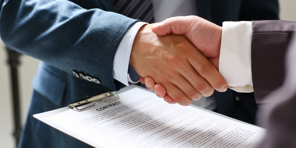 Deux personnes se serrant la main au-dessus d’un contrat signé, illustrant la conciliation d’intérêts divergents dans le cadre de Dora.