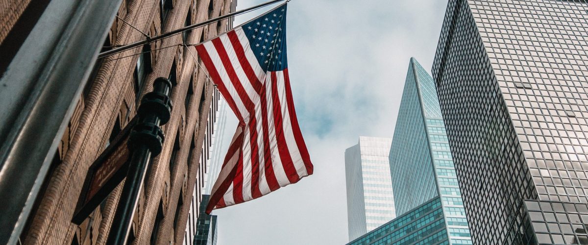 the USA or United States of America flag on a flagpole near skyscrapers under a cloudy sky Droit d’auteur : protéger au mieux votre logiciel aux États-Unis