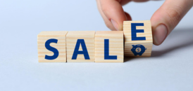 Main tenant des cubes en bois formant le mot “SALE”, illustrant les soldes et promotions e-commerce avant un webinar sur la conformité juridique et la preuve numérique.